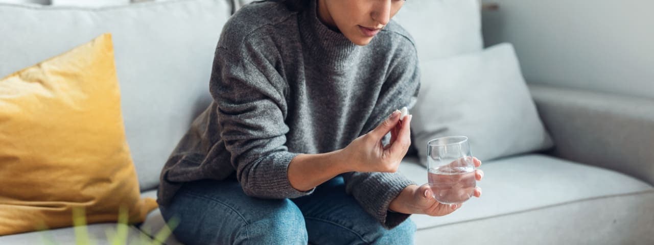 A woman sitting on a couch holding a capsule and a glass of water